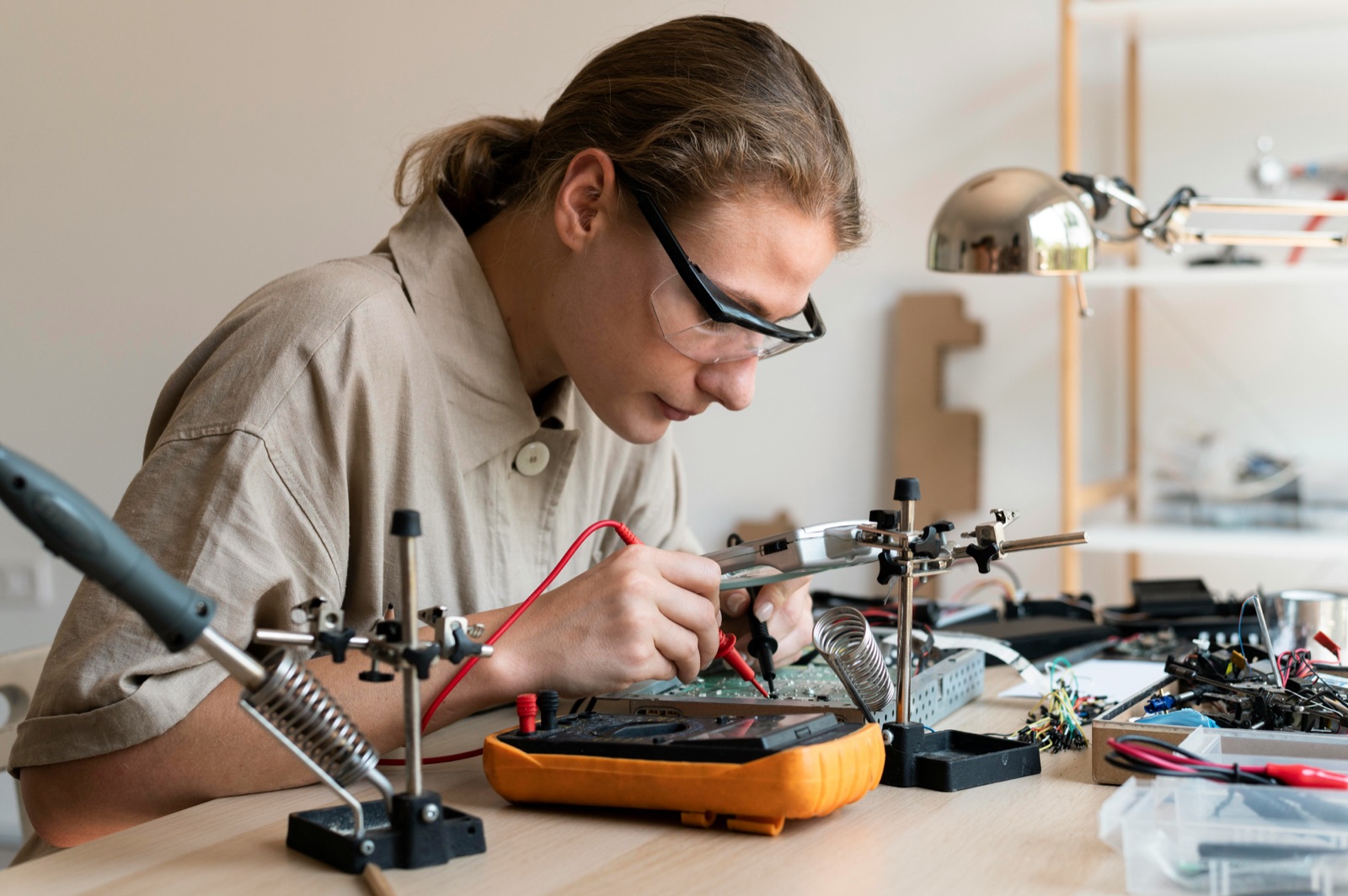 Technician with safety glasses testing PCB with multimeter for Incure Sniper™ electronics assembly