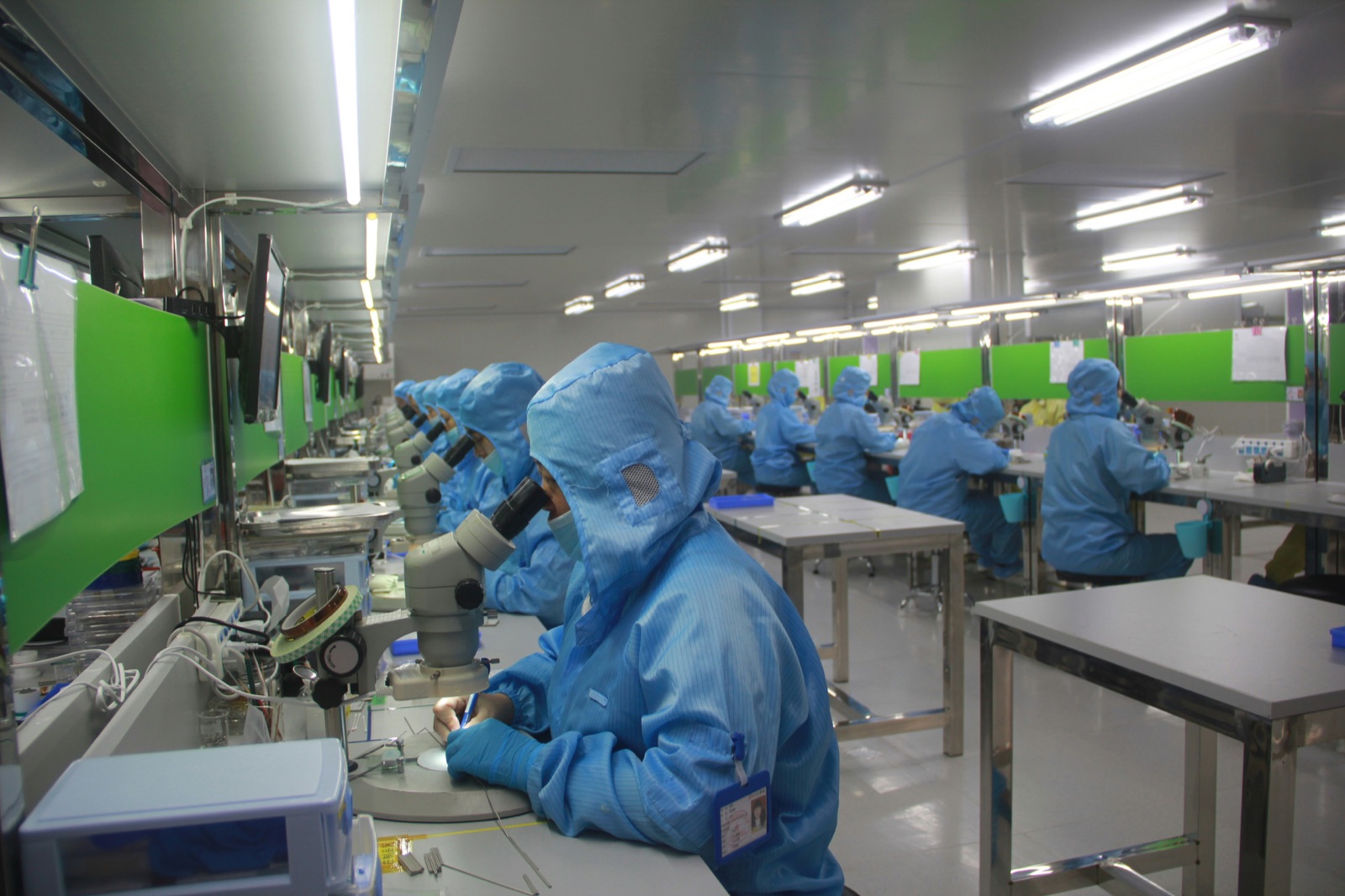 Electronics cleanroom workers in blue protective suits performing microscope inspection for Ultra-Illumina™ UV